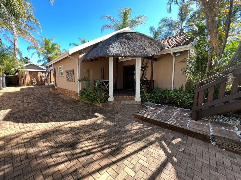 Front exterior view of the property featuring a distinctive thatched roof entrance, brick paved driveway, and established garden surroundings.