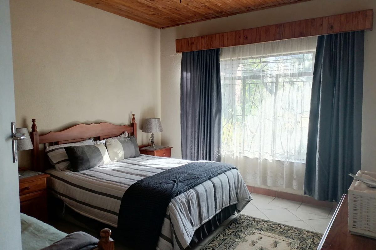 A bedroom featuring a timber ceiling, tiled flooring, and large windows with security bars, offering a functional and comfortable living space.