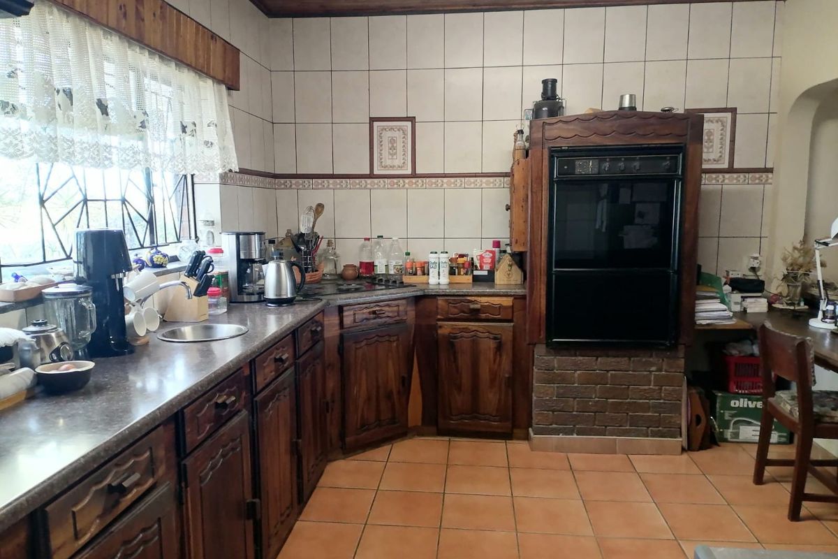 A traditional kitchen featuring dark wood cabinetry, laminate countertops, a built-in eye-level oven, and tiled flooring with a timber ceiling finish.