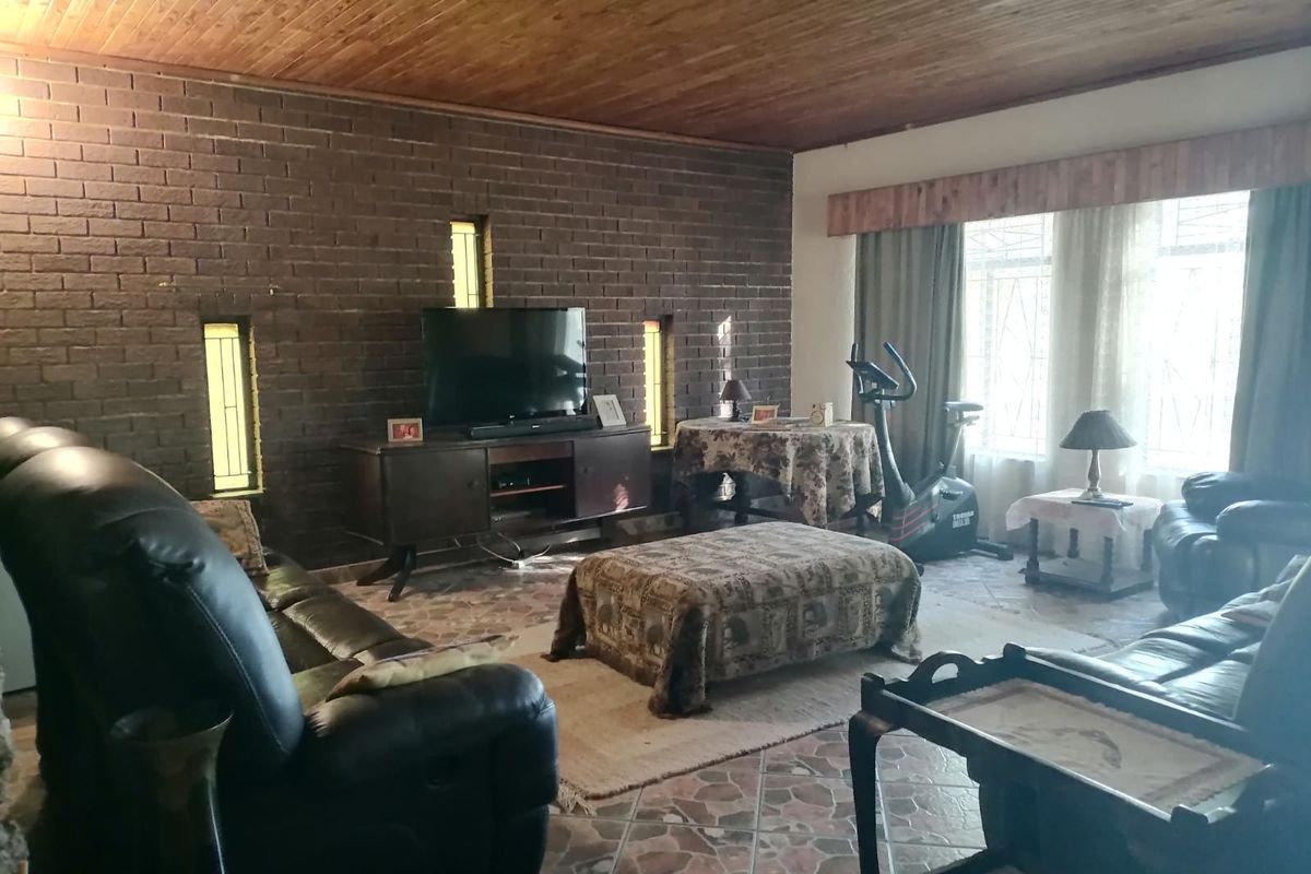 Spacious living room featuring a distinctive exposed brick wall, timber ceiling, and tiled flooring, offering a rustic aesthetic with natural light.