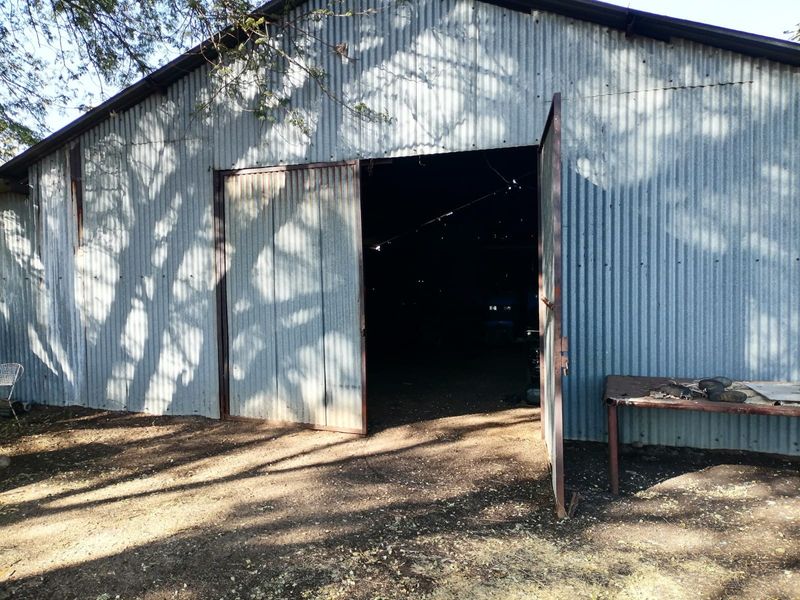 A large, rustic corrugated metal barn or workshop structure featuring wide hinged doors, suitable for storage or agricultural use on a small holding.