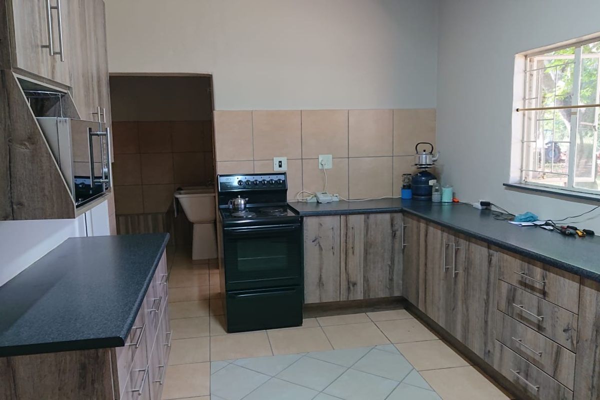 Functional kitchen featuring wood-look cabinetry, dark laminate countertops, tiled backsplash, and a freestanding stove, with an adjacent scullery area visible.