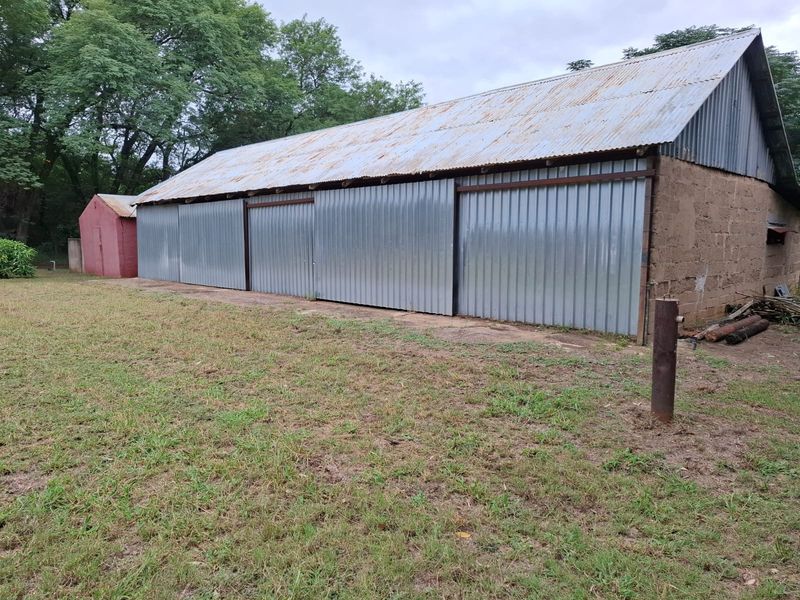 A large outbuilding or storage shed featuring corrugated iron roofing and sliding metal doors, situated on a rural small holding property.