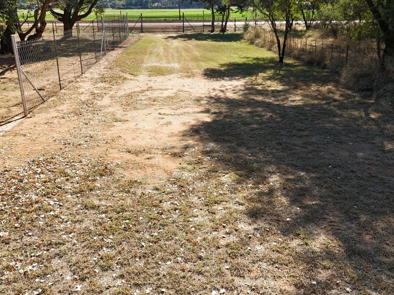 A view of the property's garden area featuring wire mesh perimeter fencing and a metal gate, with dry, sparse lawn and natural vegetation.