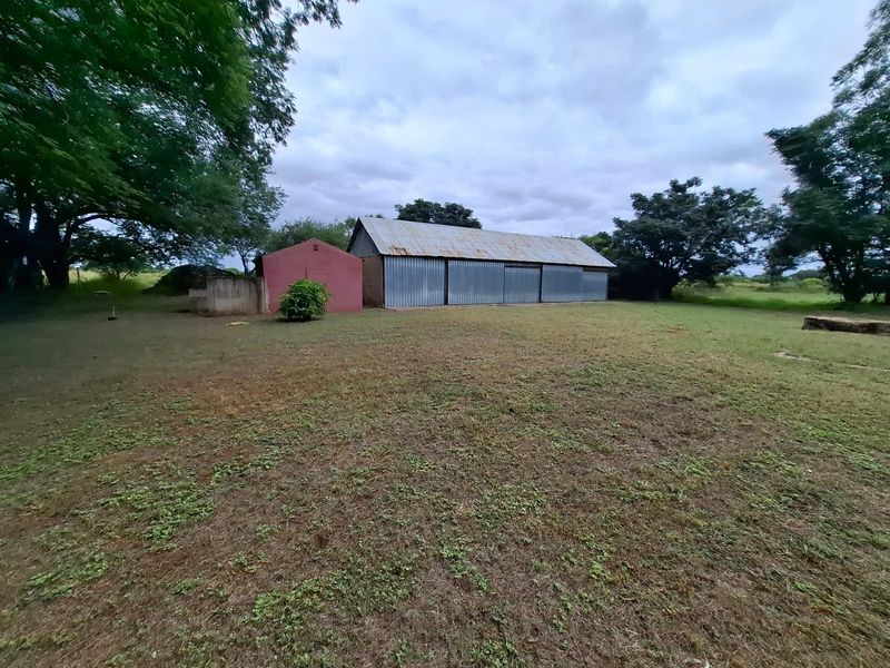 A view of the rear garden featuring a large corrugated metal outbuilding and a smaller red structure set within a spacious lawn area.