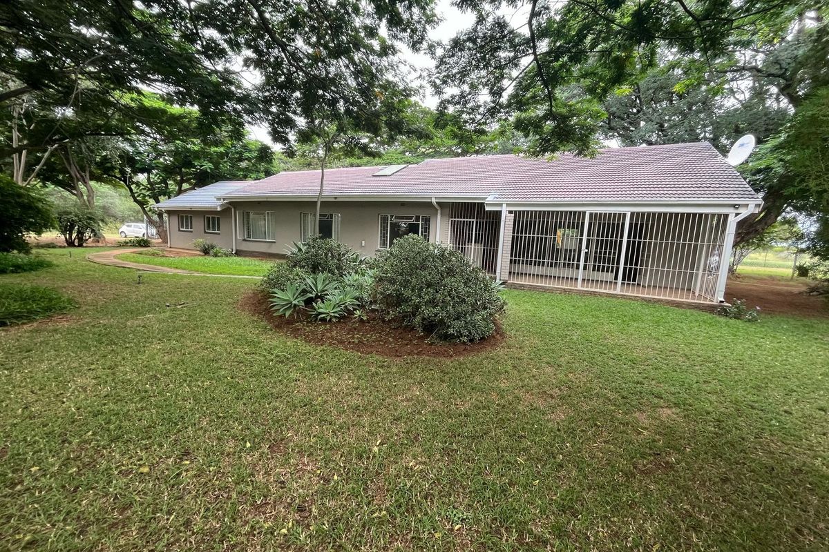 Rear view of the property featuring a tiled roof, security bars on sliding doors, and a well-maintained garden with mature trees.