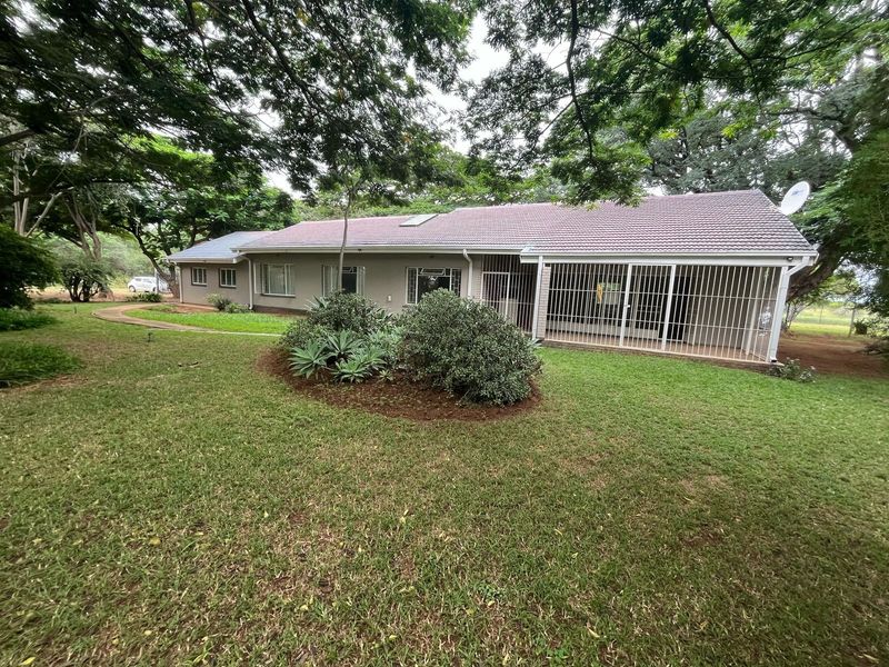 Rear view of the property featuring a tiled roof, security bars on sliding doors, and a well-maintained garden with mature trees.