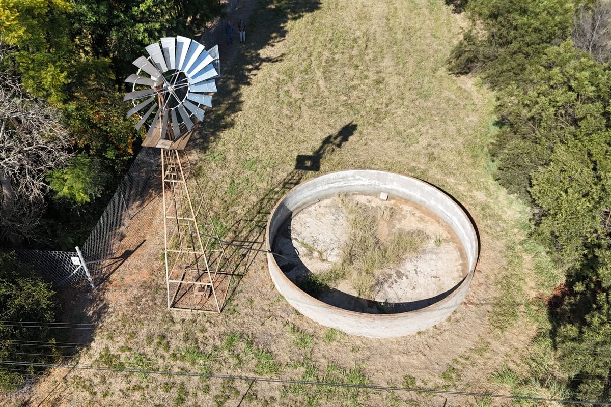 Aerial view of a small holding featuring a traditional metal windmill and a large circular concrete water reservoir.