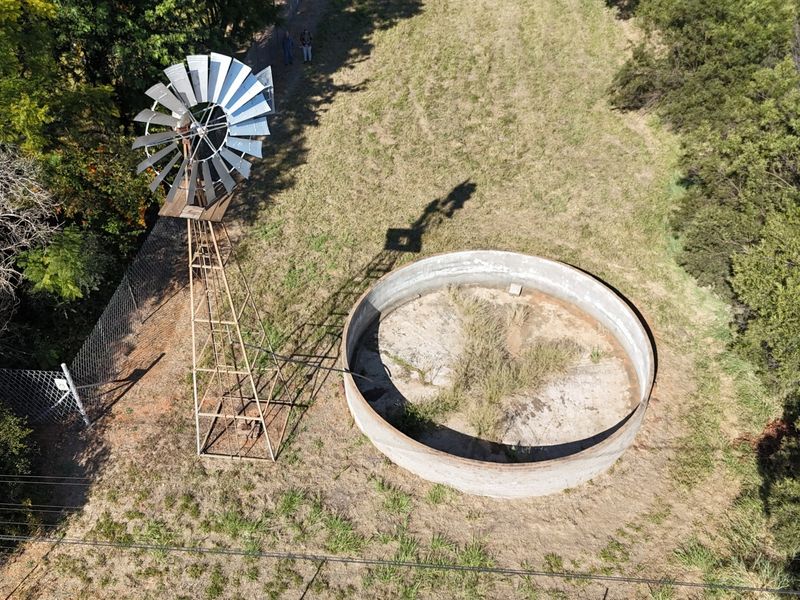 Aerial view of a small holding featuring a traditional metal windmill and a large circular concrete water reservoir.