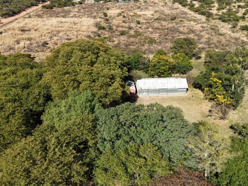 Aerial view of a small holding property featuring a structure with a corrugated metal roof surrounded by extensive mature trees and natural vegetation.