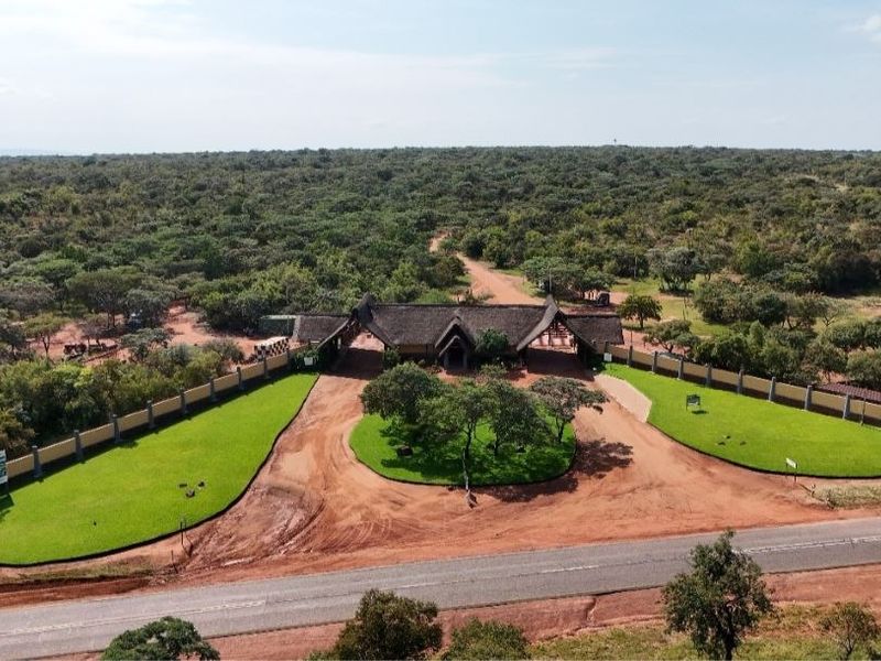 Aerial view of the property entrance featuring a thatched roof gatehouse, perimeter wall, and well-maintained landscaped grounds.