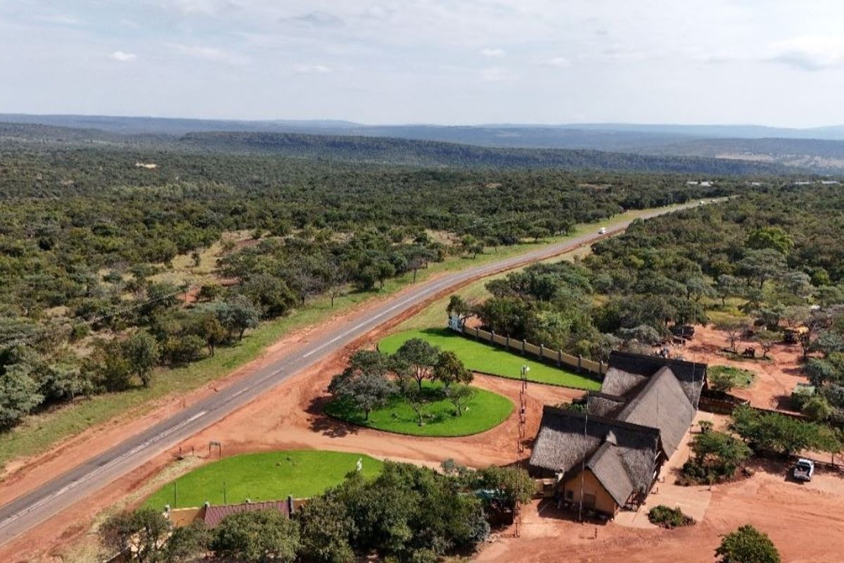 Aerial view of a residential property featuring a thatched-roof building, landscaped grounds, and direct access to a paved road in a rural setting.