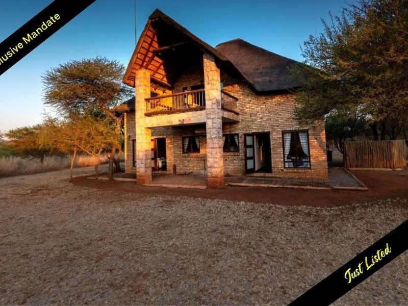 A two-story house featuring traditional thatched roofing, stone exterior cladding, and a covered balcony overlooking the surrounding natural landscape.