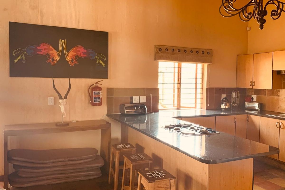A functional kitchen featuring granite countertops, wooden cabinetry, and a built-in hob, with a breakfast bar area and tiled flooring.