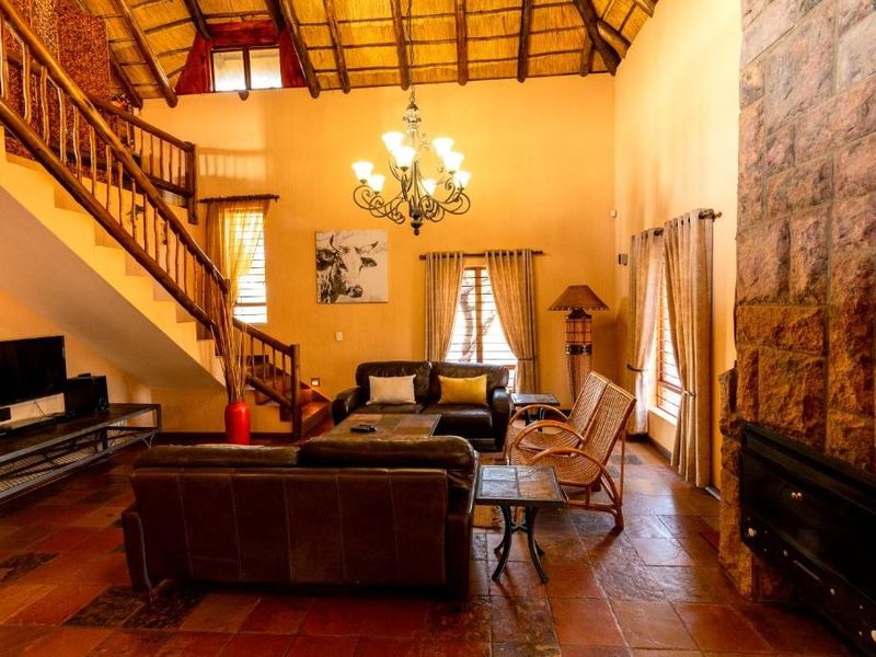 Spacious living room featuring a double-volume thatched ceiling with exposed rafters, a prominent stone fireplace, and traditional terracotta floor tiles.