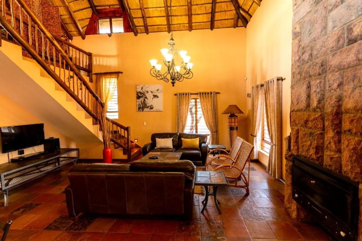 Spacious living room featuring a double-volume thatched ceiling with exposed rafters, a prominent stone fireplace, and traditional terracotta floor tiles.