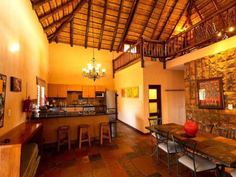 Spacious open-plan living and dining area featuring a high thatched roof with exposed timber trusses, a stone feature wall, and a mezzanine level.
