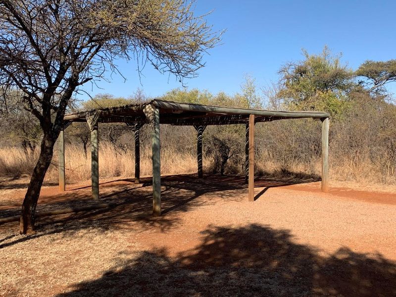 An open-air timber and thatch gazebo structure set within a natural bushveld environment, providing a shaded outdoor area.