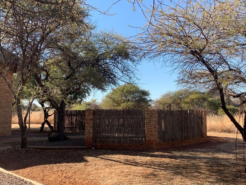 A natural garden area featuring a brick and timber slat enclosure, mature trees, and a paved pathway set within a rural landscape.