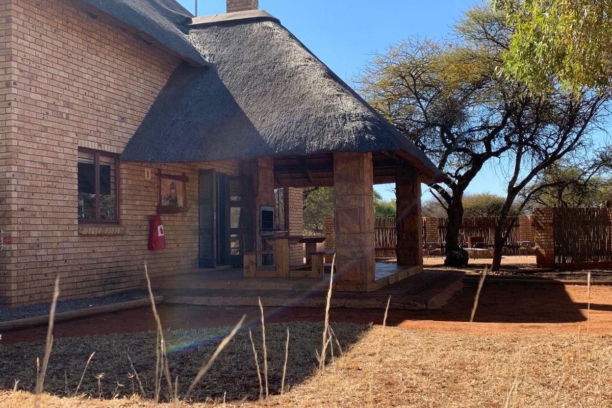 Rear view of a brick house featuring a thatched roof and a covered patio area with a built-in braai.