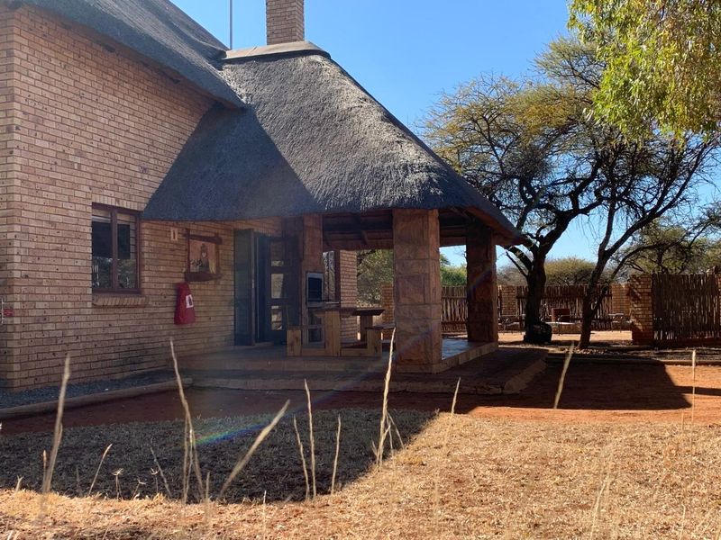 Rear view of a brick house featuring a thatched roof and a covered patio area with a built-in braai.