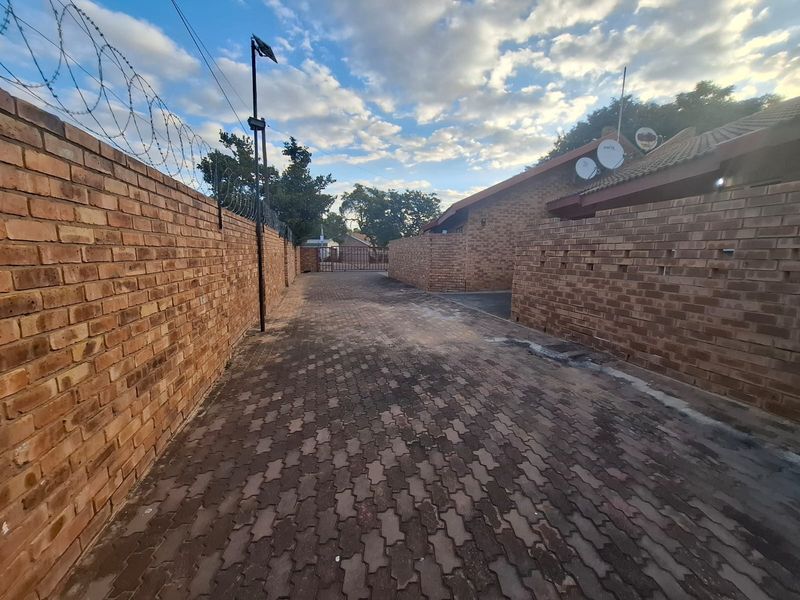 A view of the paved driveway and brick boundary walls with security razor wire, leading towards the entrance of the townhouse property.
