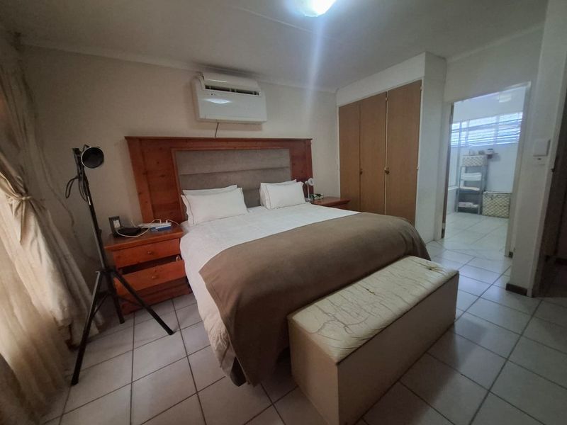 A bedroom featuring tiled flooring, built-in cupboards, and an integrated air conditioning unit, with an adjoining bathroom visible.