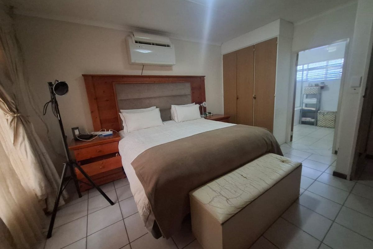 A bedroom featuring tiled flooring, built-in cupboards, and an integrated air conditioning unit, with an adjoining bathroom visible.