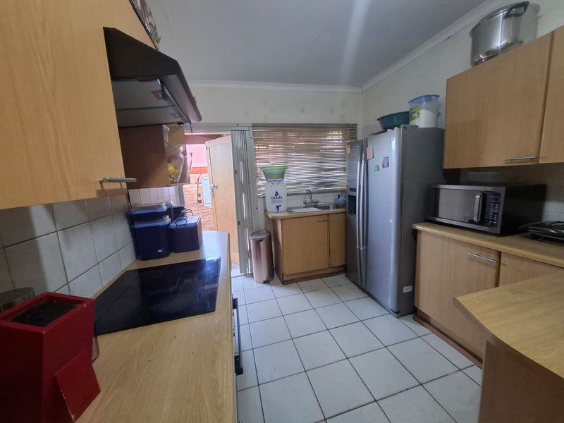 A functional kitchen featuring laminate cabinetry, tiled flooring, a built-in electric hob with extractor fan, and a stainless steel sink with a window view.