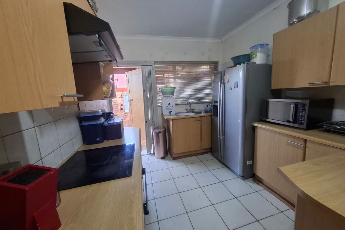 A functional kitchen featuring laminate cabinetry, tiled flooring, a built-in electric hob with extractor fan, and a stainless steel sink with a window view.