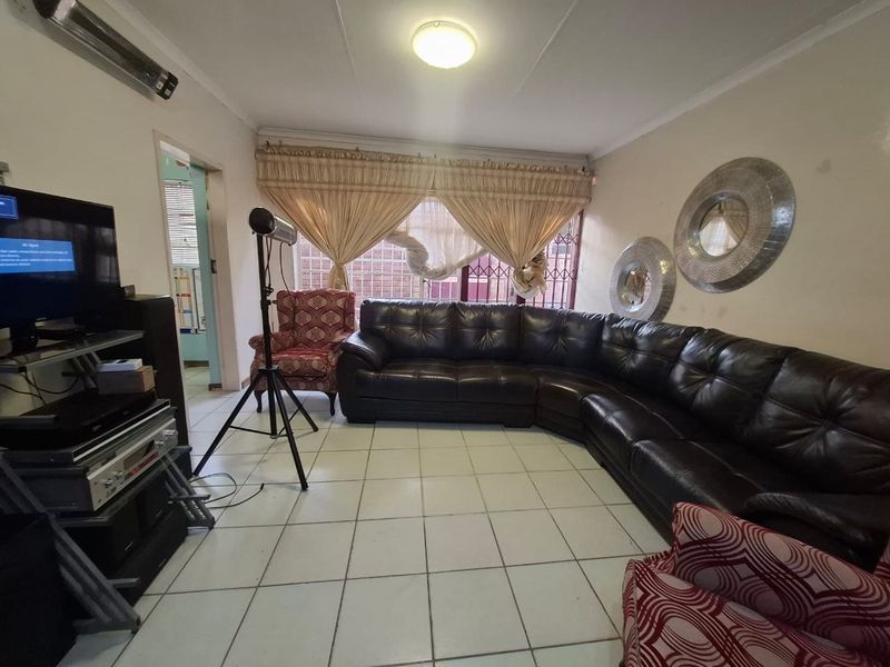 A living room featuring ceramic floor tiles and a window with security bars, offering a functional space in need of cosmetic updates.
