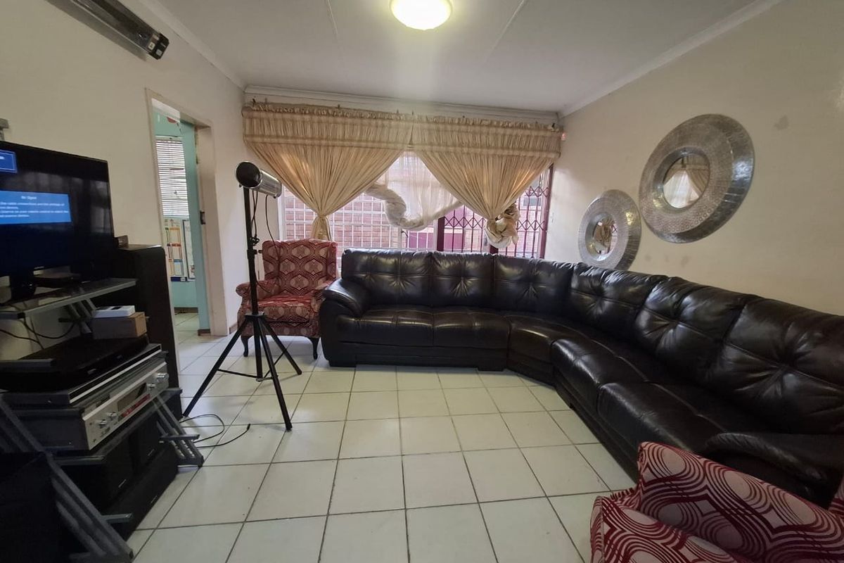 A living room featuring ceramic floor tiles and a window with security bars, offering a functional space in need of cosmetic updates.