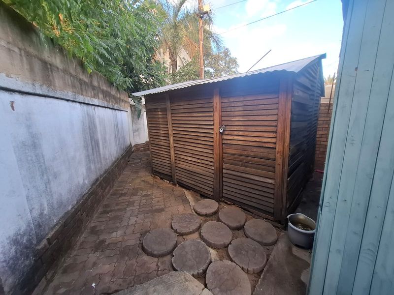 A functional outdoor utility area featuring a wooden storage shed situated on a paved walkway alongside a boundary wall.