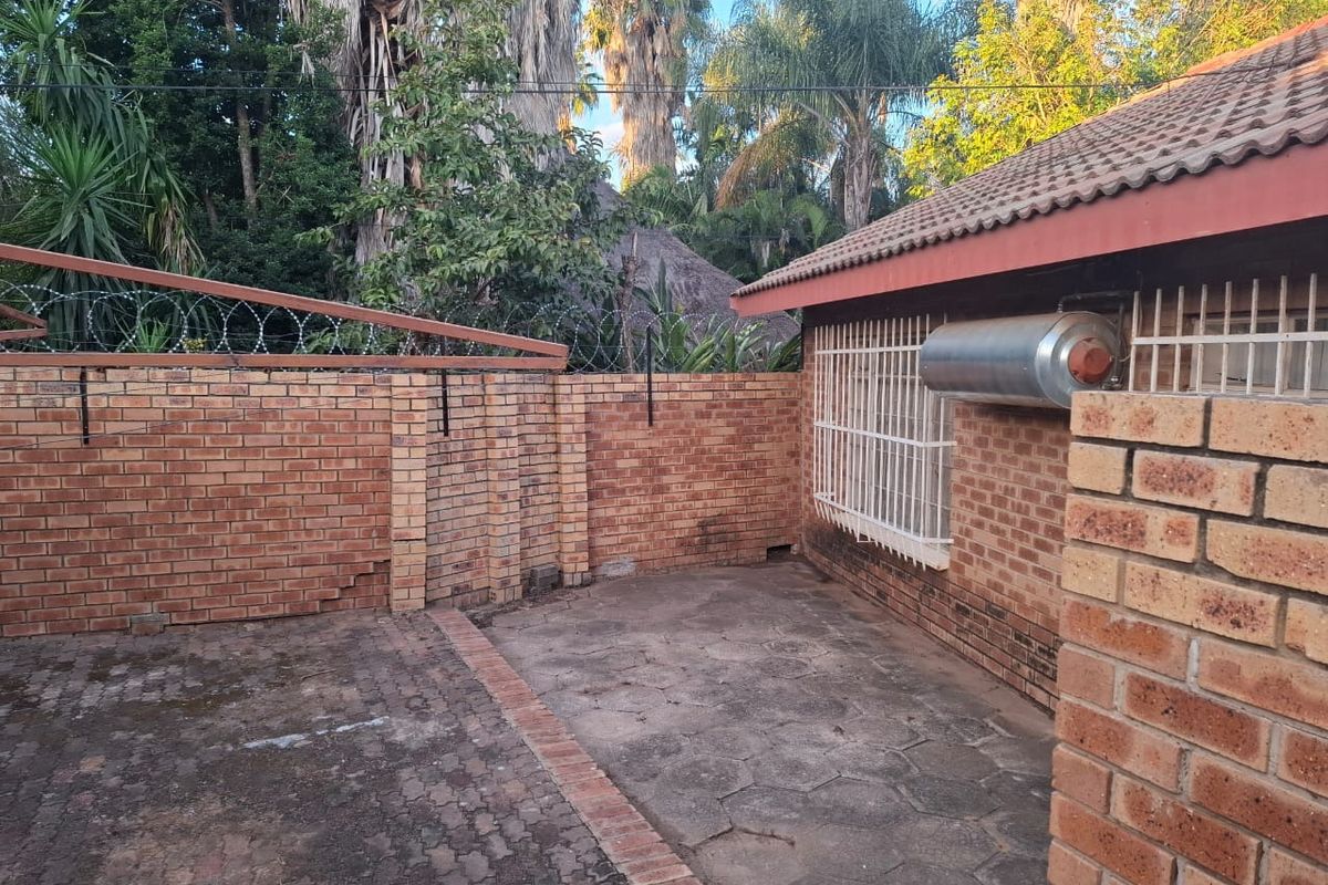 A private rear courtyard featuring brick boundary walls with security fencing, paved flooring, and an external geyser unit attached to the townhouse structure.