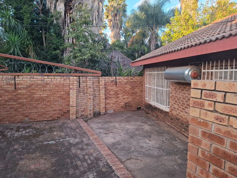 A private rear courtyard featuring brick boundary walls with security fencing, paved flooring, and an external geyser unit attached to the townhouse structure.
