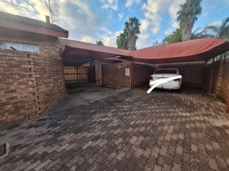 Front exterior view of the townhouse featuring a brick facade, paved driveway, and a covered carport area.