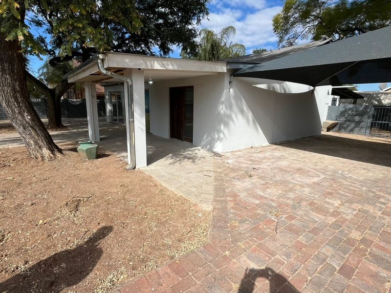 Rear exterior view featuring a paved driveway, covered patio area, and shade sail structure within a fenced garden setting.