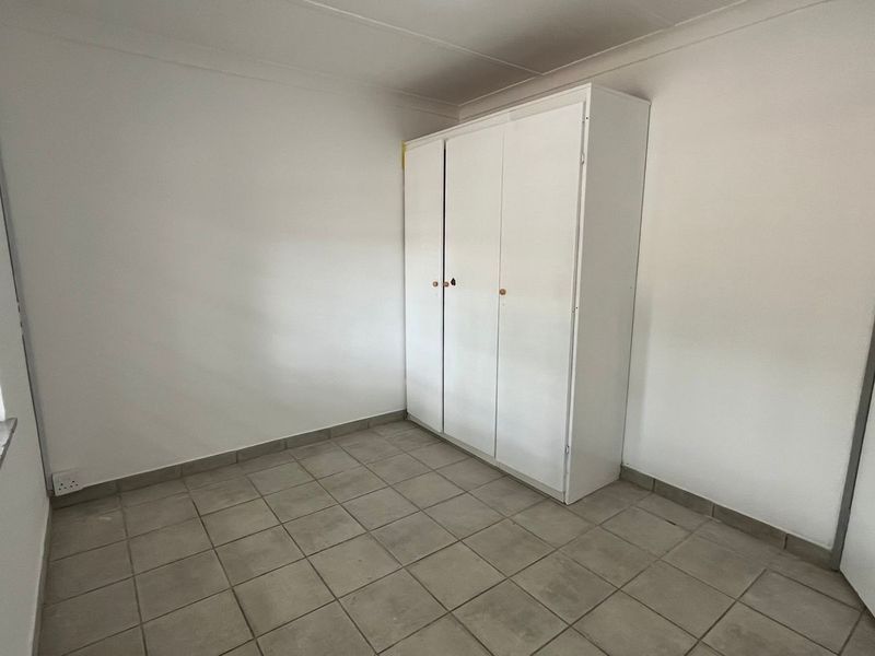 A simple, empty bedroom featuring tiled flooring, a built-in wardrobe, and security bars on the window.