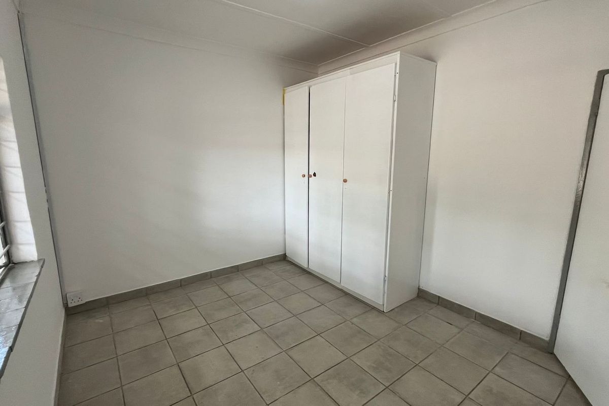 A simple, empty bedroom featuring tiled flooring, a built-in wardrobe, and security bars on the window.