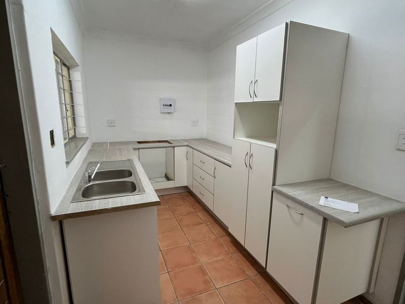 A functional kitchen space featuring white cabinetry, laminate countertops, a double bowl sink, and tiled flooring, currently awaiting appliance installation.
