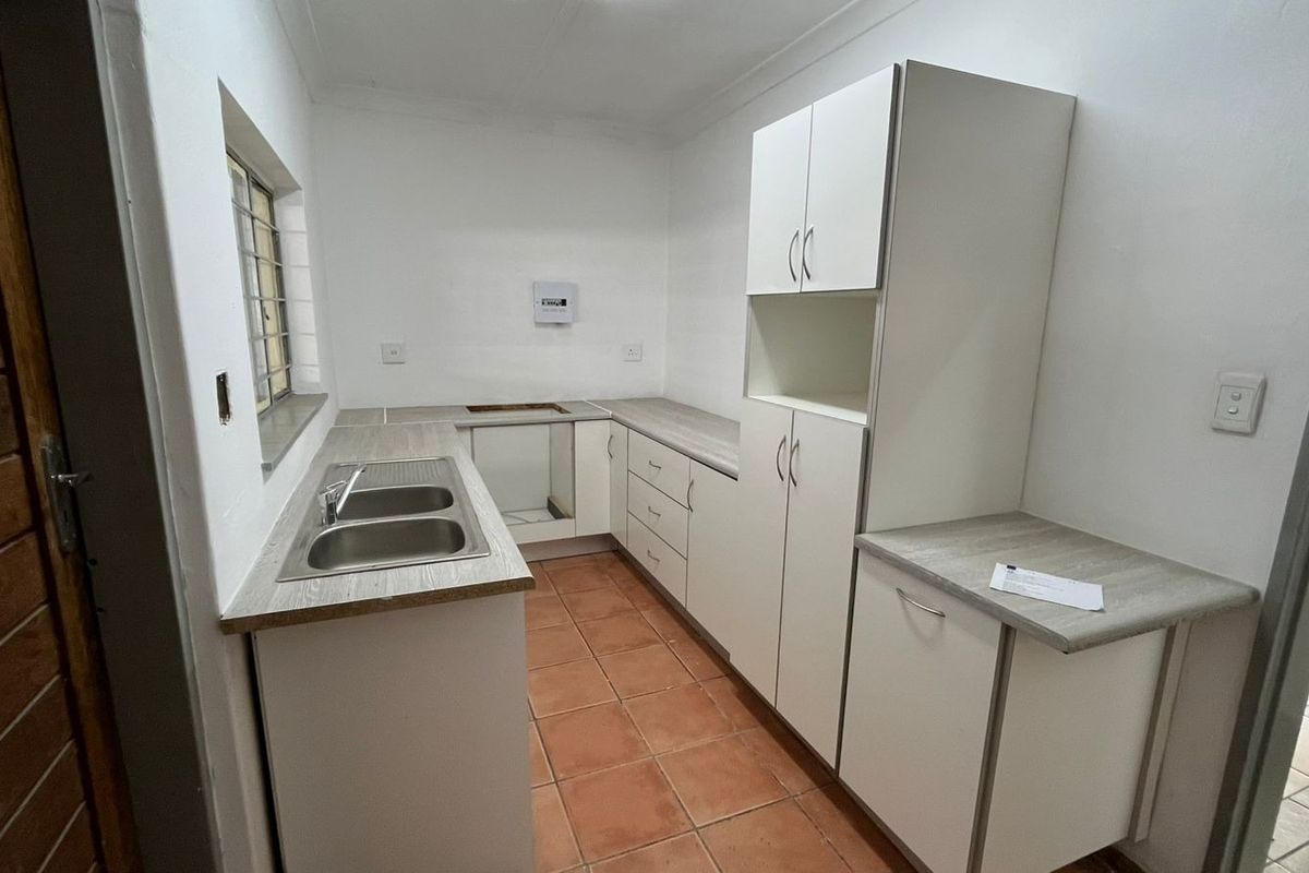 A functional kitchen space featuring white cabinetry, laminate countertops, a double bowl sink, and tiled flooring, currently awaiting appliance installation.