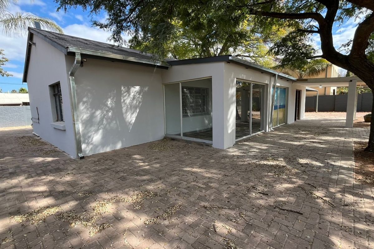 Rear view of the property featuring a paved courtyard area, large sliding glass doors, and a covered patio space under mature trees.