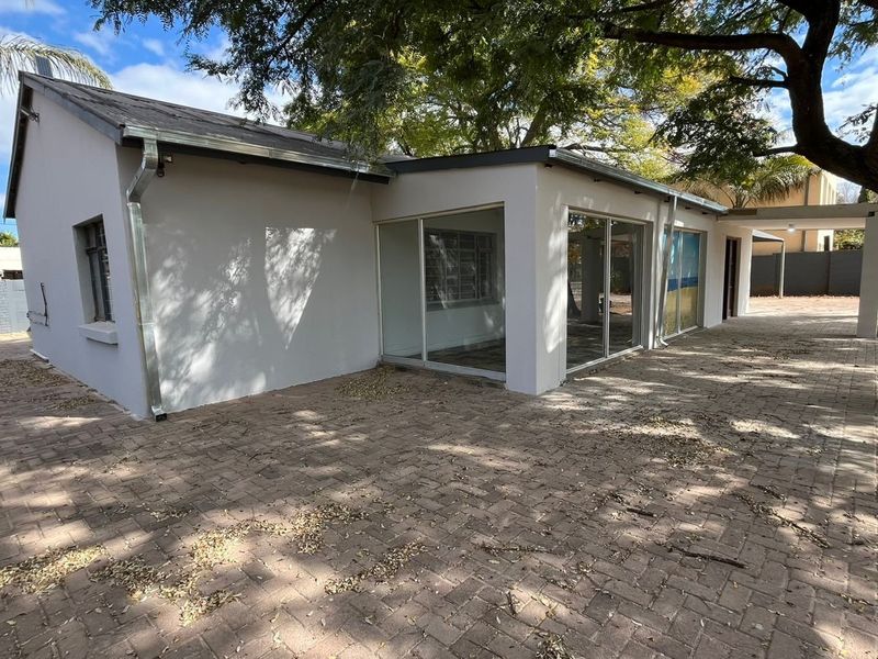 Rear view of the property featuring a paved courtyard area, large sliding glass doors, and a covered patio space under mature trees.
