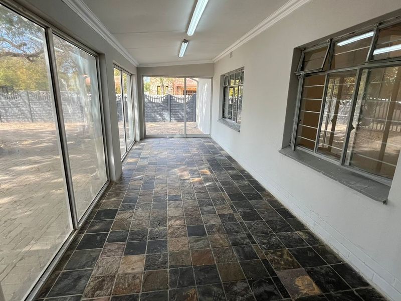 A spacious, enclosed patio area featuring slate tile flooring, large sliding glass doors, and ample natural light, suitable for a sunroom or entertainment space.