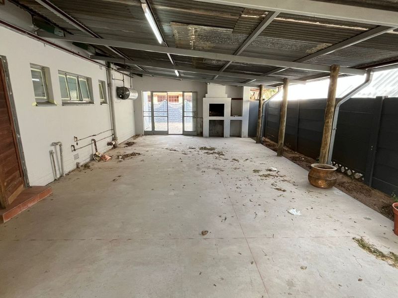 A spacious covered patio area featuring a built-in braai, concrete flooring, and timber support posts, offering a blank canvas for outdoor entertainment.