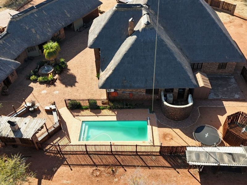 Aerial view of a property featuring a thatched roof house, a swimming pool, and a paved courtyard area.