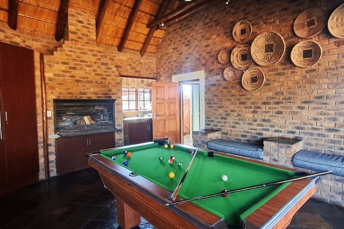 Spacious entertainment room featuring exposed brick walls, a high thatched ceiling, built-in fireplace, and integrated brick seating with slate flooring.