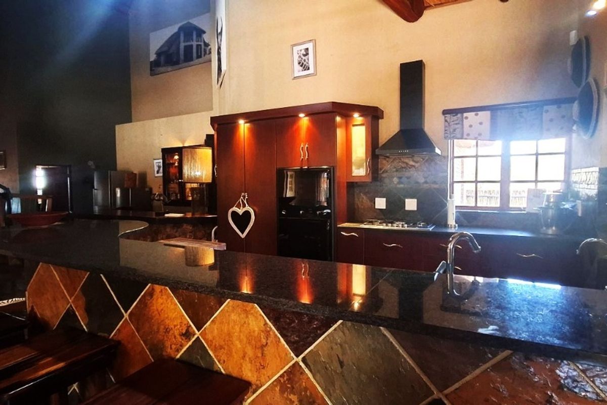 Spacious kitchen featuring dark wood cabinetry, granite countertops, a tiled breakfast bar, and exposed timber beams, offering a rustic and functional cooking space.