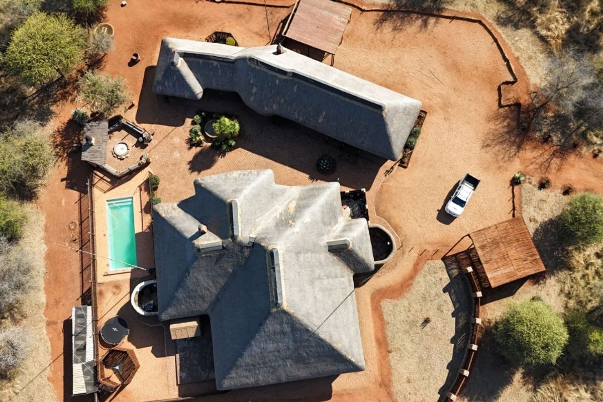 Aerial view of a property featuring multiple thatched-roof structures, a swimming pool, and surrounding natural landscape.