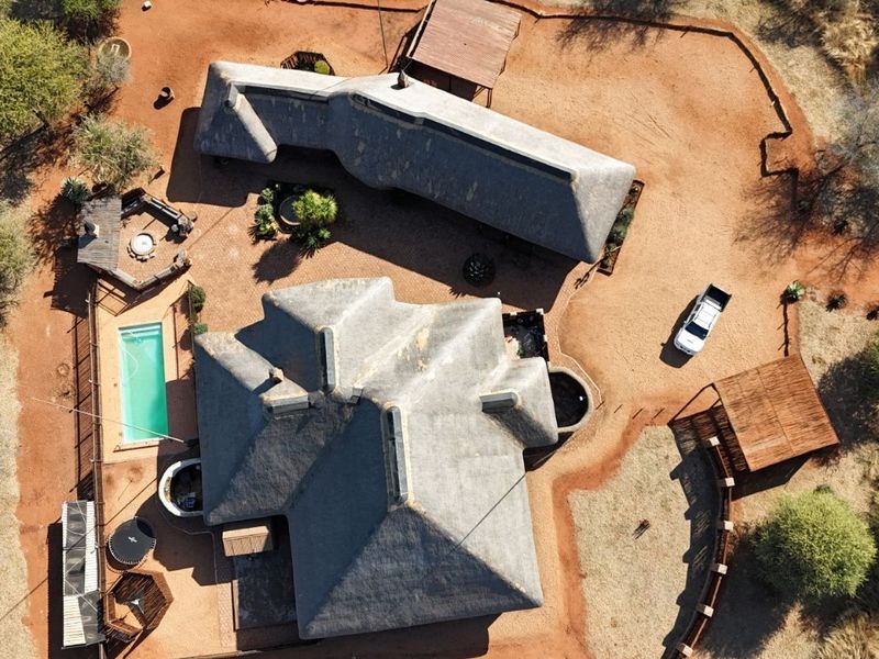 Aerial view of a property featuring multiple thatched-roof structures, a swimming pool, and surrounding natural landscape.